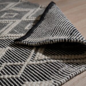 Black and cream geometric rug with raised diamond texture shown folded on light wood flooring.