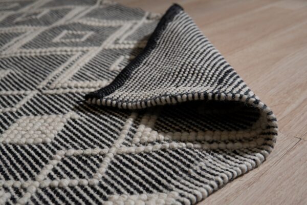 Black and cream geometric rug with raised diamond texture shown folded on light wood flooring.
