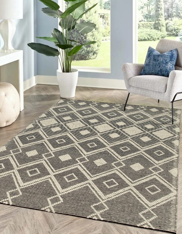 Black and off-white geometric diamond rug anchors a living area with a gray chair and herringbone wood floor.