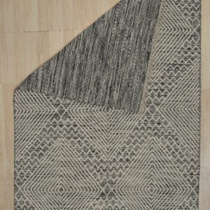 Textured black and beige rug with geometric pattern, folded over on light wood planks.