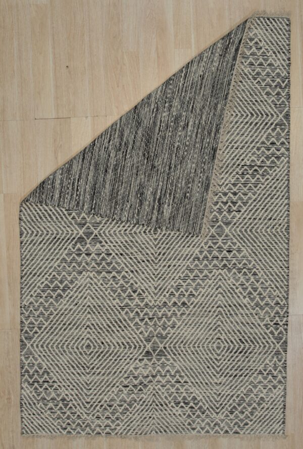 Textured black and beige rug with geometric pattern, folded over on light wood planks.