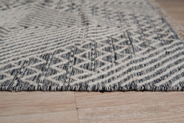Black and off-white geometric rug with textured zigzags and stripes lies on light wood plank flooring.