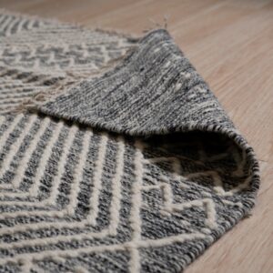 Close-up of a curled gray and white geometric textured rug on light wood flooring.