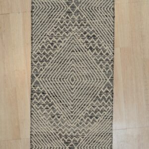 Black and beige diamond and chevron motifs cover this textured runner rug on a light wood floor.