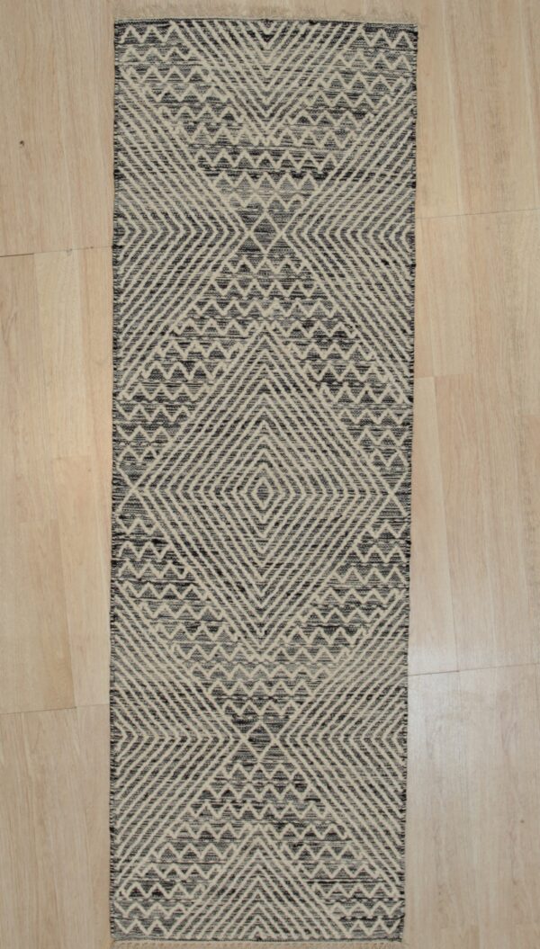 Black and beige diamond and chevron motifs cover this textured runner rug on a light wood floor.