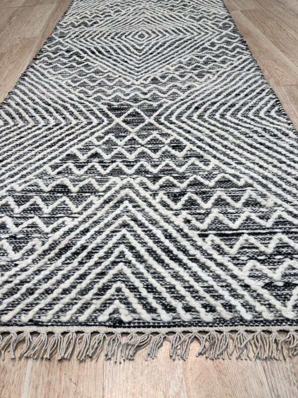 Black and white textured runner rug with fringe and geometric patterns on a light wood floor.