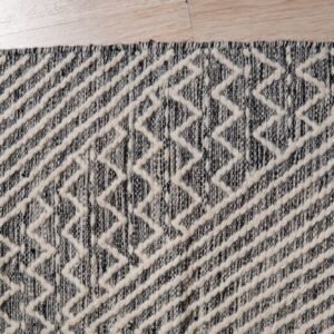 Raised cream geometric zigzags overlay a dark speckled rug with fringe on light wood flooring.