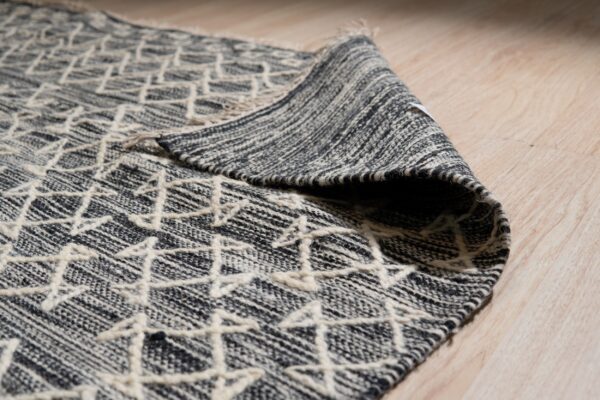 Textured gray and cream rug with a raised geometric pattern sits partially rolled on light wood plank flooring.