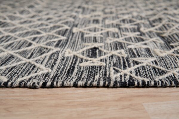 Close-up of a black and cream low-pile rug with raised geometric lines on light wood flooring.