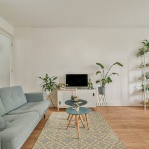 A low-pile gray and yellow geometric rug grounds a light blue sofa and wooden flooring.