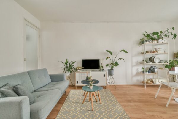 A low-pile gray and yellow geometric rug grounds a light blue sofa and wooden flooring.