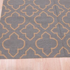 Low-pile gray rug featuring a repeating tan geometric trellis pattern rests on light blonde wood flooring.