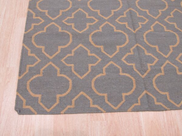 Low-pile gray rug featuring a repeating tan geometric trellis pattern rests on light blonde wood flooring.