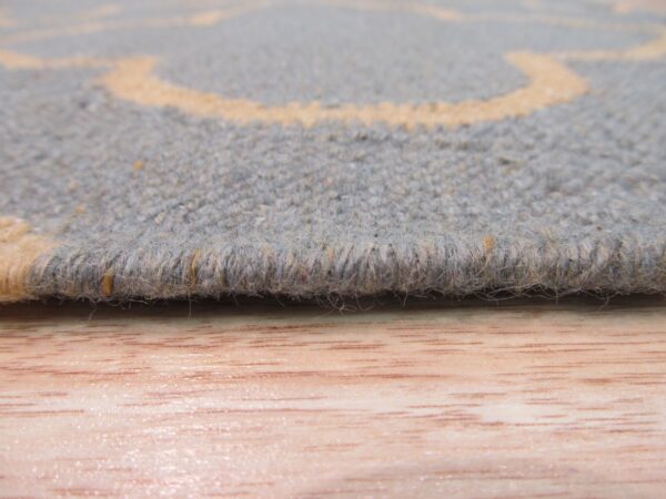 Textured gray-blue rug edge with pale orange accents rests on a light wood floor surface.