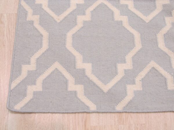 Low-pile rug with a repeating light blue and cream geometric trellis pattern on light wood floor.