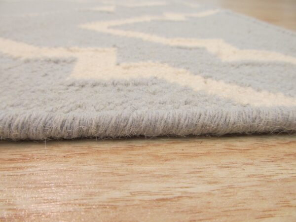 The high-pile edge of a gray and white zigzag rug rests on light-toned, glossy wood planks.