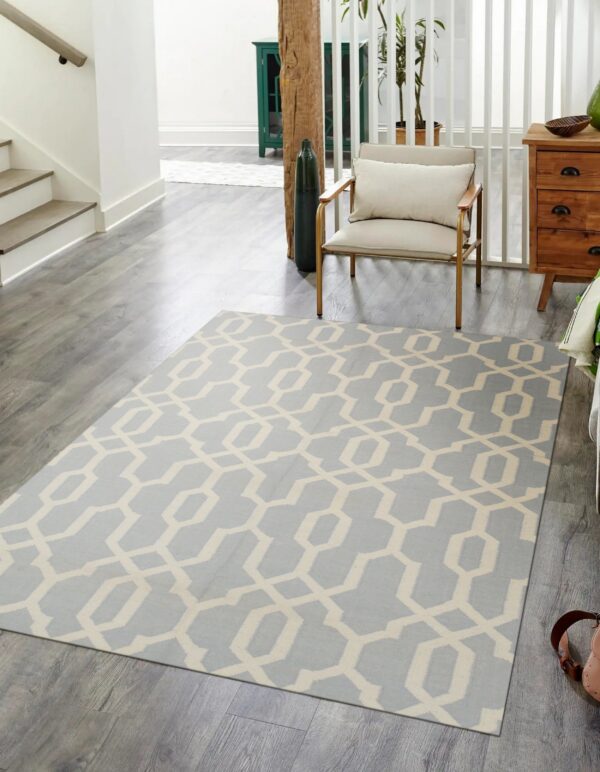 Light blue and cream geometric rug on grey wood floors in a bright hallway near a chair.