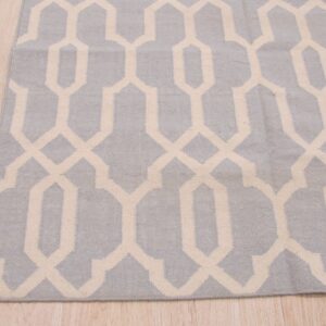 A low-pile blue-gray rug with a cream interlocking geometric pattern covers light wood flooring.