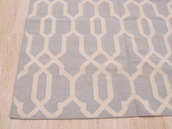 A low-pile blue-gray rug with a cream interlocking geometric pattern covers light wood flooring.