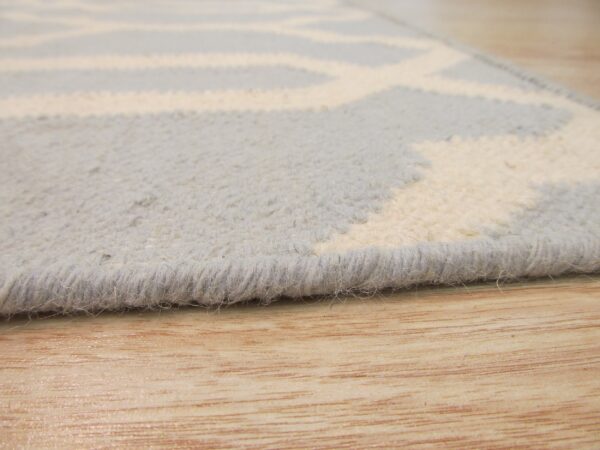 Close-up view of a textured light blue and ivory geometric rug resting on light wood flooring.