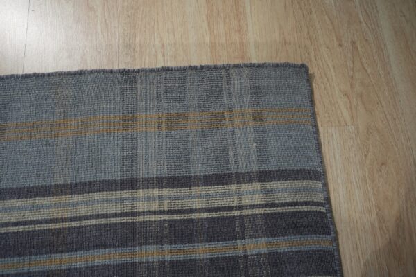 Muted gray and blue flatweave rug with beige plaid stripes rests on light wood flooring.