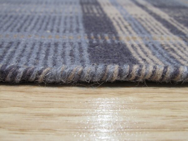 Close-up of a ribbed blue and gray plaid rug edge resting on glossy light wood flooring.