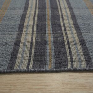 Close-up of a low-pile plaid rug featuring blue, charcoal, beige, and tan stripes on light wood flooring.