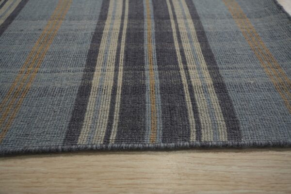 Close-up of a low-pile plaid rug featuring blue, charcoal, beige, and tan stripes on light wood flooring.