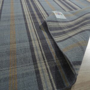 A flat-weave rug with blue, gray, and tan vertical stripes is partially rolled on light wood flooring.