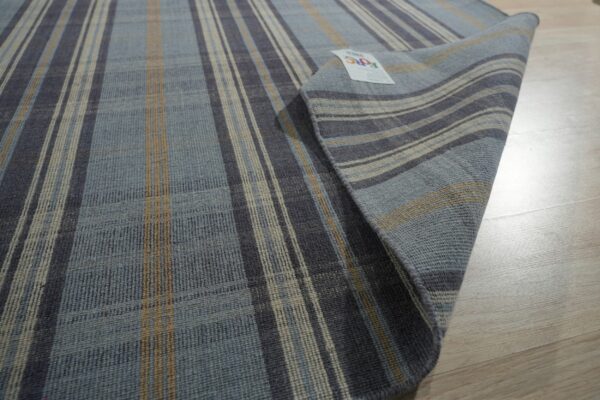 A flat-weave rug with blue, gray, and tan vertical stripes is partially rolled on light wood flooring.