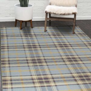 Slate blue, mustard, and brown plaid rug on dark wood flooring by a white brick wall.