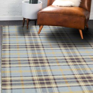 Light blue plaid rug with yellow and dark brown stripes anchors a brown leather chair near a brick wall.
