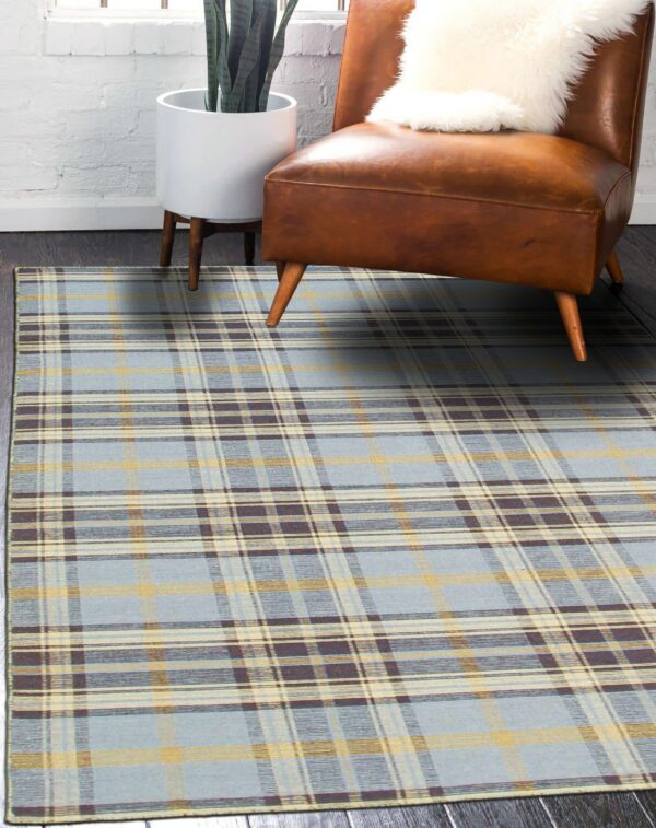 Light blue plaid rug with yellow and dark brown stripes anchors a brown leather chair near a brick wall.