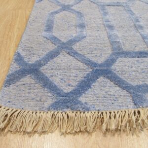 Close-up of a blue geometric rug with visible light beige fringe laying on light wood flooring.