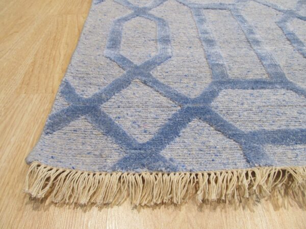 Close-up of a blue geometric rug with visible light beige fringe laying on light wood flooring.