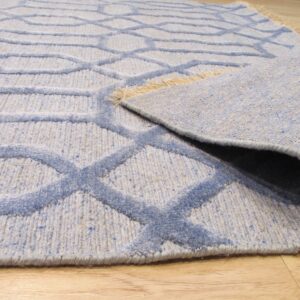 Light blue geometric rug with raised pile pattern, partially rolled on light wood planks.