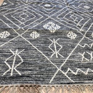 A textured black and white rug featuring a bold diamond pattern and fringe lays on light hardwood flooring.