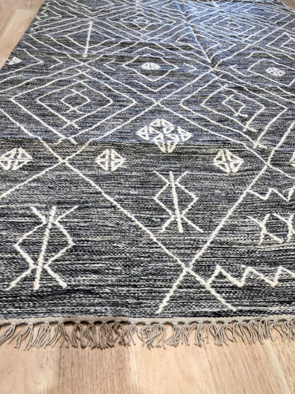 A textured black and white rug featuring a bold diamond pattern and fringe lays on light hardwood flooring.