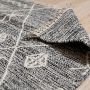 A heathered gray rug featuring thick, raised white geometric patterns and tassels lies on light wood flooring.