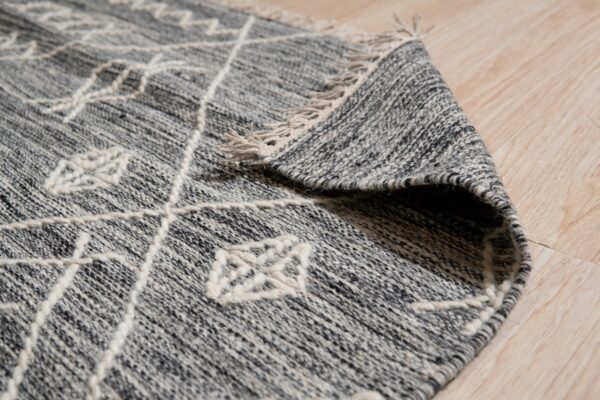 A heathered gray rug featuring thick, raised white geometric patterns and tassels lies on light wood flooring.