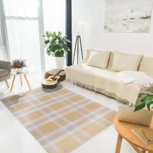 A tan and blue plaid rug grounds a bright living room with white floors, a beige sofa, and a grey armchair.