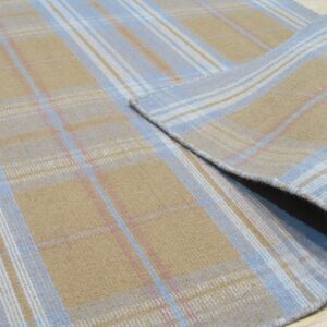 Tan and light blue plaid rug with pink accents, displaying a flat texture partially rolled up on wood flooring.