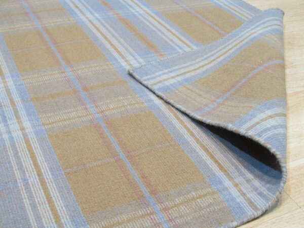 Tan and light blue plaid rug with pink accents, displaying a flat texture partially rolled up on wood flooring.