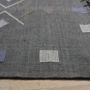 Dark gray flatweave rug with blue, white, and gold geometric patterns on light wood floor.