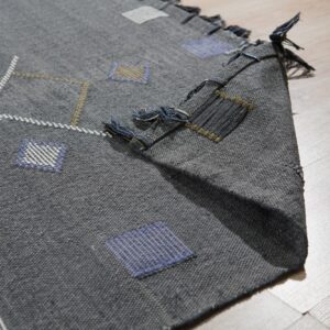 Gray flatweave rug with geometric blue, white, and khaki patterns, folded over on light wood flooring.