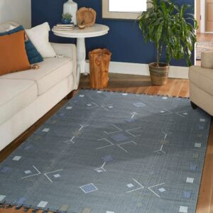 Geometric blue and gray flat-weave rug with tassels grounds a living room with cream furniture and wood floors.