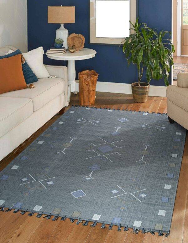 Geometric blue and gray flat-weave rug with tassels grounds a living room with cream furniture and wood floors.
