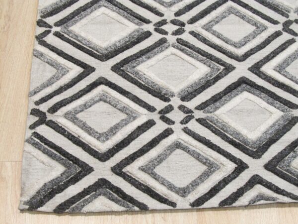 Black, gray, and white textured rug with geometric diamonds resting on light wood floor.