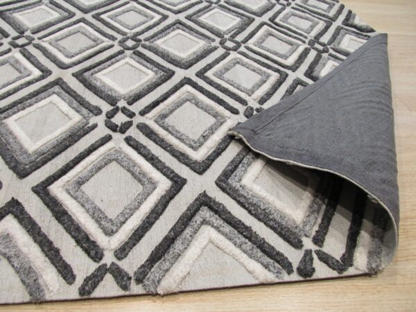 Textured gray geometric rug showing raised diamond pile and a folded dark gray backing on wood floor.