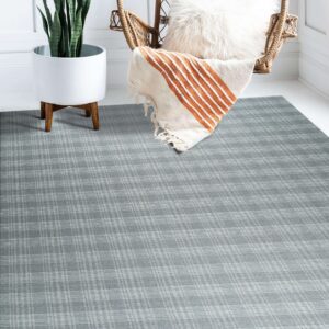 Low pile gray plaid rug covers white wood floors next to a plant and wicker chair.